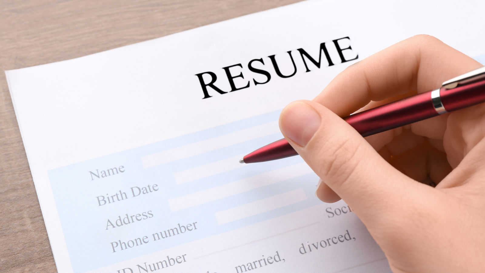 Hand holding a red pen over a blank resume form with fields for name, address and phone number