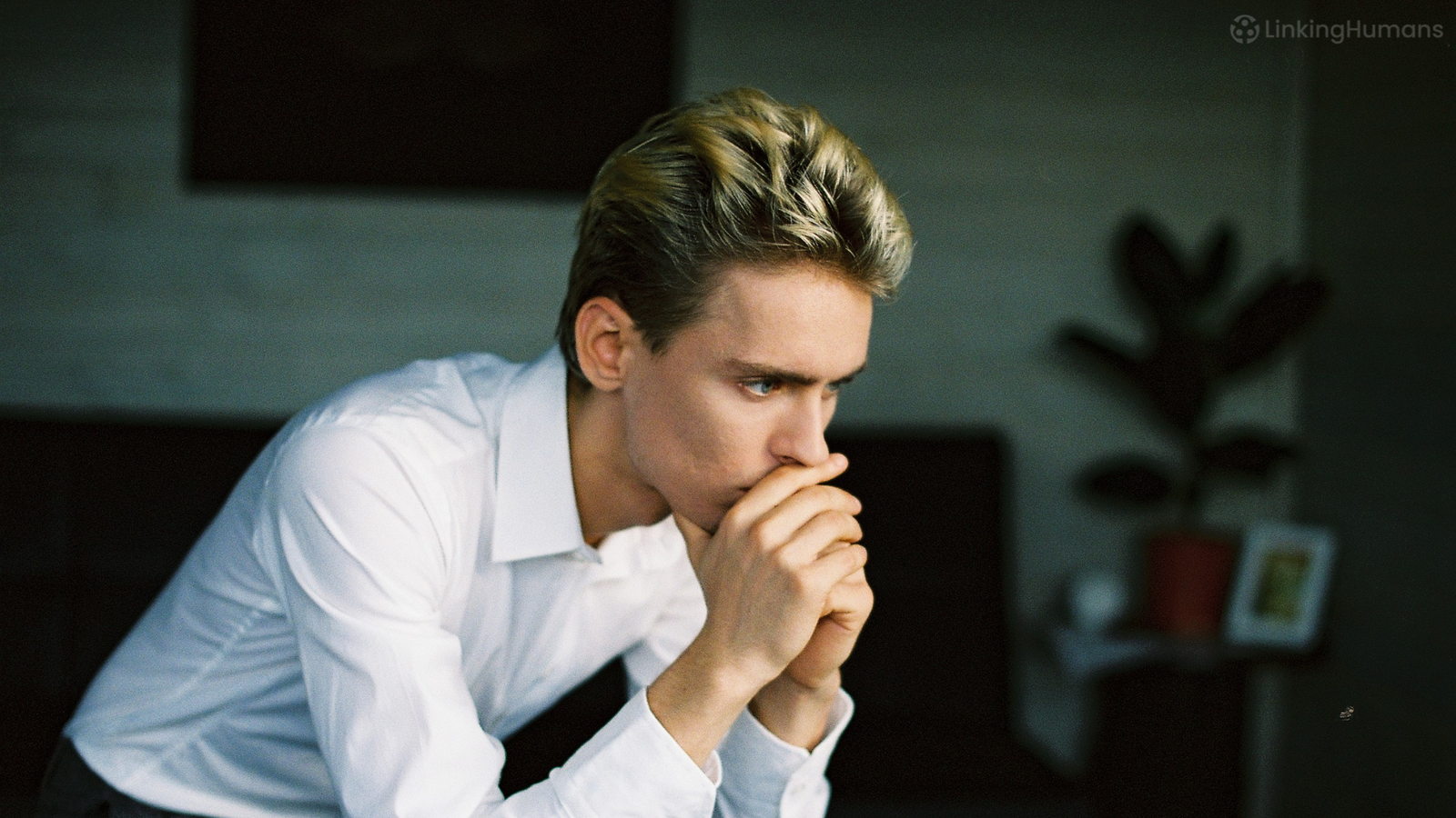 Young man in a white shirt sitting with hands clasped to his mouth, looking anxious before an interview