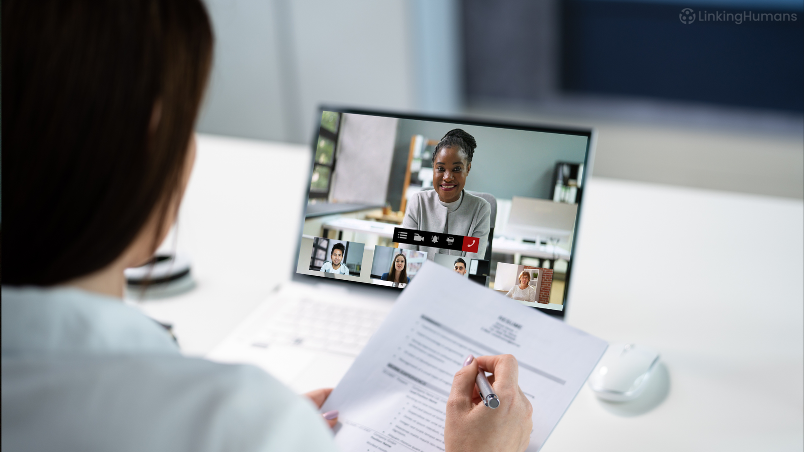 Recruiter reviewing a printed CV during a video interview with candidates on a laptop screen
